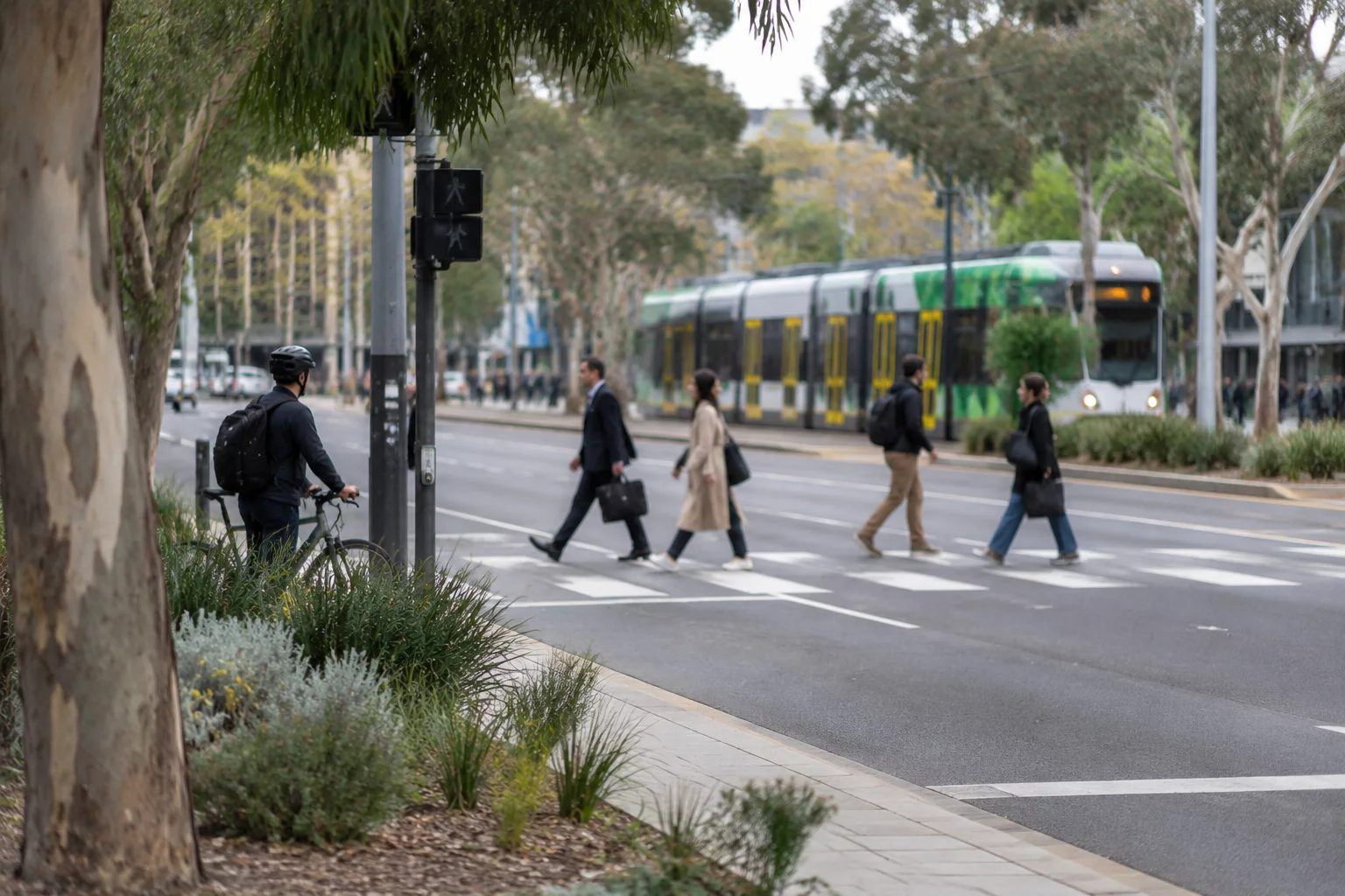 Commuters crossing a city street in morning light, with a tram and a cyclist behind them